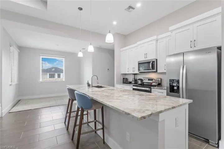 Kitchen featuring stainless steel appliances, white cabinets, a kitchen island with sink, light stone countertops, and a kitchen bar