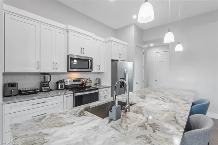 Kitchen with stainless steel appliances, white cabinets, decorative light fixtures, and recessed lighting