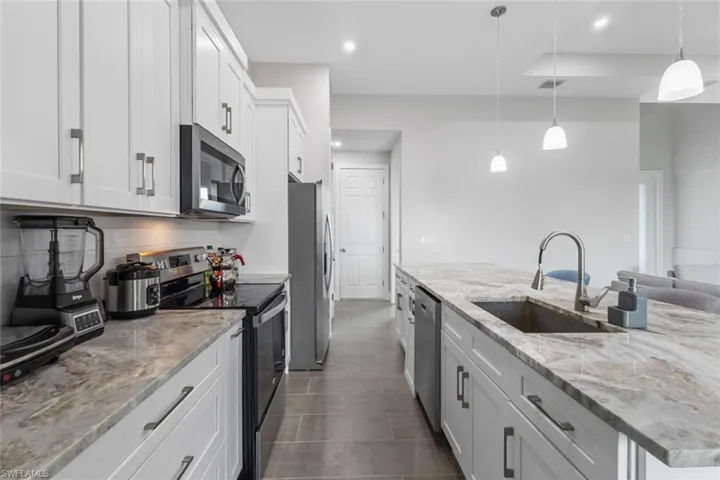Kitchen featuring appliances with stainless steel finishes, white cabinetry, recessed lighting, decorative light fixtures, and light stone counters