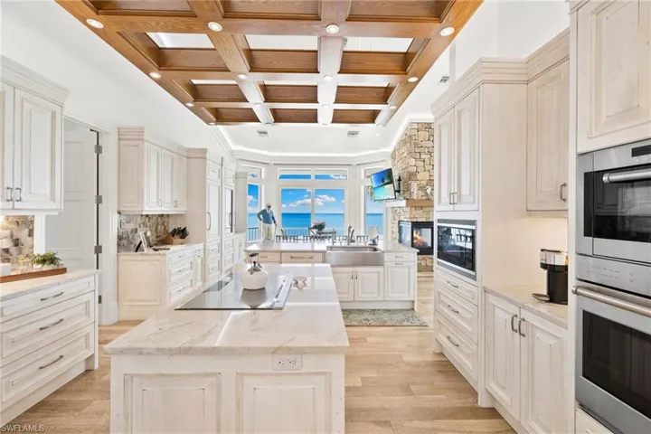 Kitchen featuring coffered ceiling, black appliances, a kitchen island, beamed ceiling, and light wood-style floors