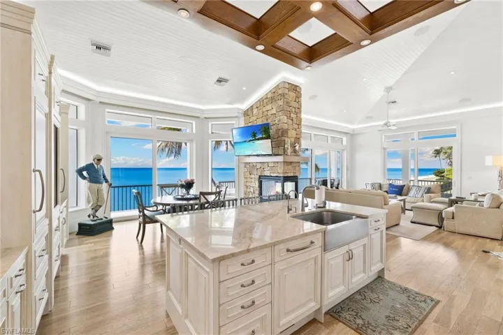 Kitchen featuring light stone countertops, coffered ceiling, open floor plan, a stone fireplace, and beamed ceiling