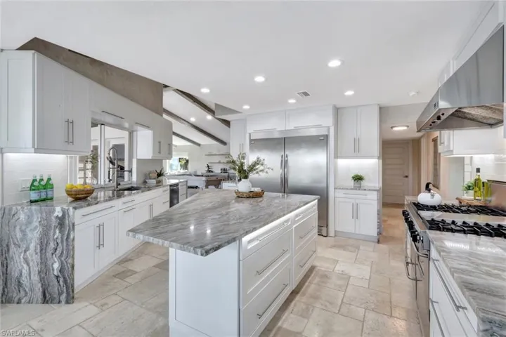 Kitchen featuring light stone counters, stainless steel appliances, exhaust hood, white cabinetry, and a large island