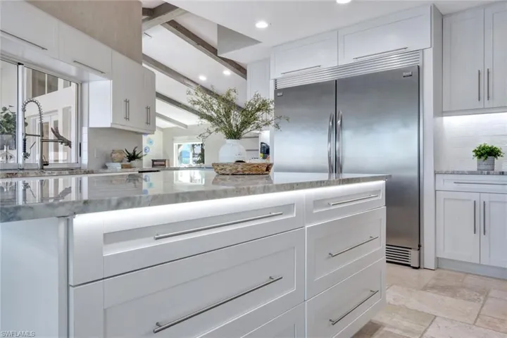 Kitchen featuring beam ceiling, built in refrigerator, white cabinets, and light stone counters