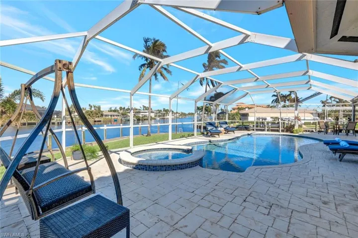 View of swimming pool with glass enclosure, an in ground hot tub, a water view, and a patio