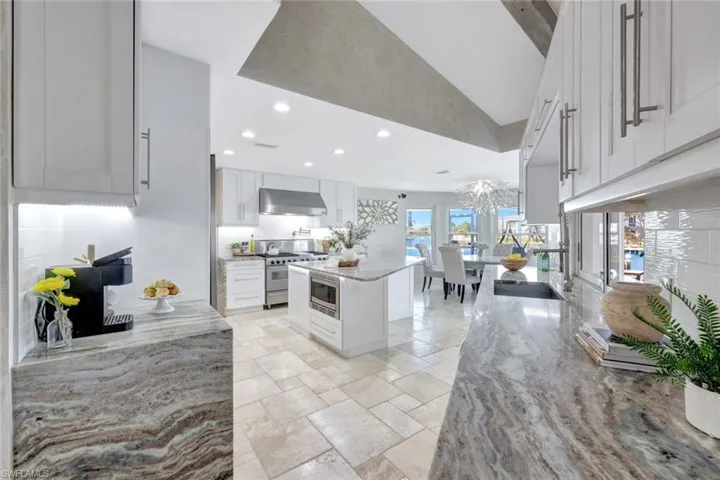 Kitchen with light stone counters, stainless steel appliances, extractor fan, a kitchen island, and white cabinetry