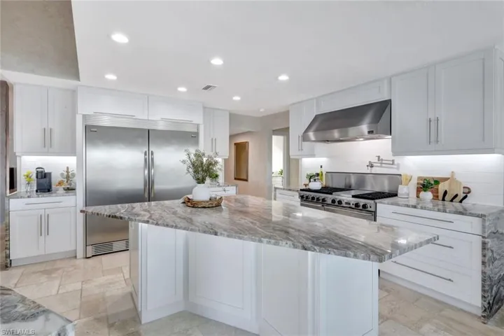 Kitchen featuring high quality appliances, white cabinets, and wall chimney range hood