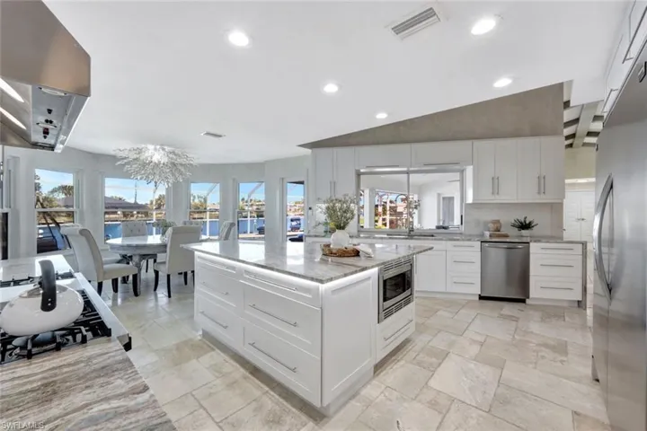 Kitchen with light stone countertops, appliances with stainless steel finishes, white cabinetry, a notable chandelier, and a kitchen island