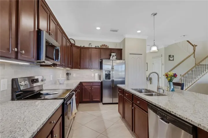 Kitchen with stainless steel appliances, light stone counters, crown molding, hanging light fixtures, and light tile patterned floors