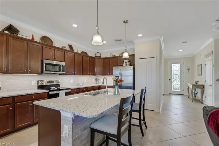 Kitchen with a kitchen bar, stainless steel appliances, light stone countertops, ornamental molding, and a center island with sink