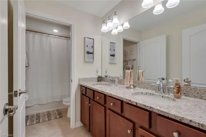 Full bathroom featuring double vanity, shower / tub combo, and light tile patterned flooring
