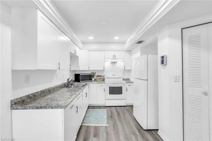 Kitchen featuring white appliances, sink, light stone countertops, light hardwood / wood-style floors, and white cabinetry