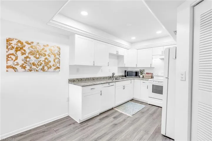 Kitchen with white cabinets, light wood-type flooring, and white appliances