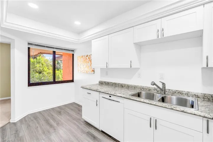 Kitchen with dishwasher, white cabinets, sink, light wood-type flooring, and light stone counters