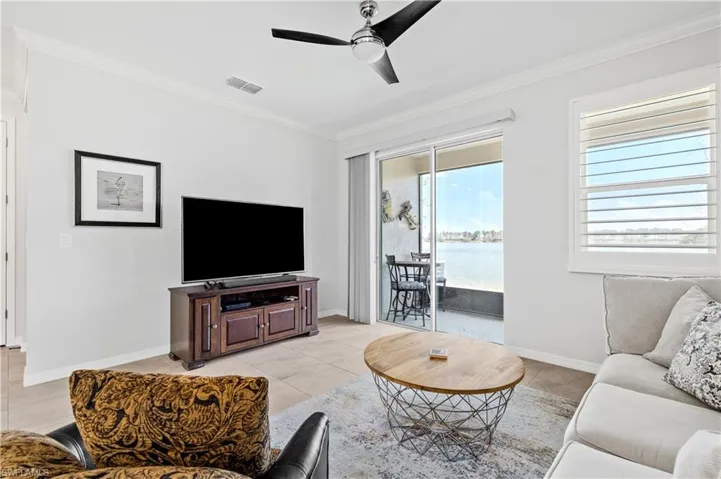 Living area with light tile patterned floors, a ceiling fan, visible vents, baseboards, and crown molding