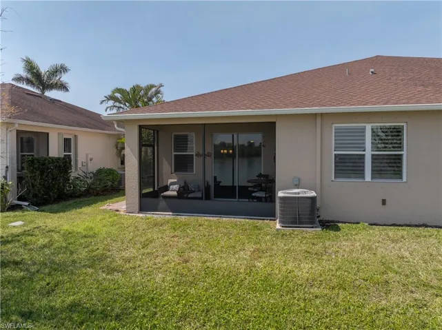 Rear view of house featuring stucco siding, central air condition unit, a shingled roof, a yard, and a sunroom