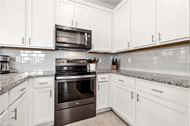 Kitchen featuring backsplash, appliances with stainless steel finishes, and white cabinetry