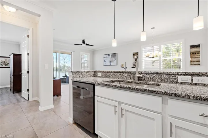 Kitchen with light stone counters, light tile patterned floors, ornamental molding, a sink, and dishwasher
