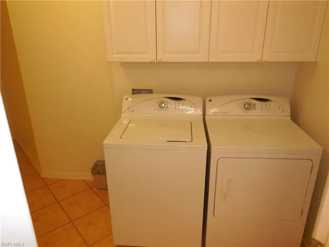 Laundry room with light tile patterned floors, washer and clothes dryer, and cabinet space