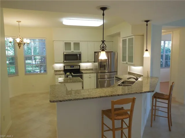 Kitchen featuring a peninsula, stainless steel appliances, glass insert cabinets, white cabinetry, and a kitchen breakfast bar