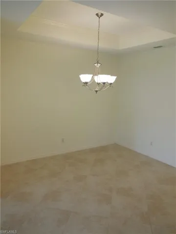 Unfurnished room with a tray ceiling, hanging lights, and crown molding