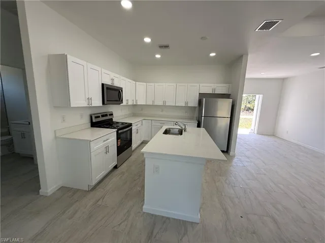 Kitchen featuring stainless steel appliances, white cabinetry, a kitchen island with sink, light stone counters, and recessed lighting