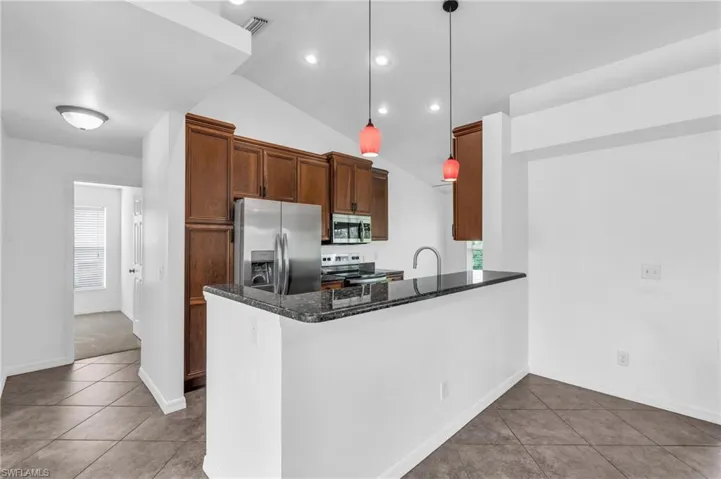Kitchen with decorative light fixtures, appliances with stainless steel finishes, kitchen peninsula, lofted ceiling, and dark stone counters
