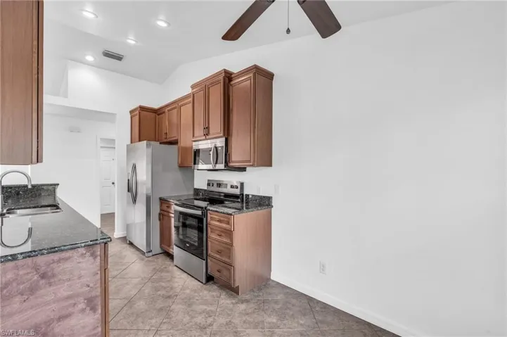 Kitchen featuring dark stone countertops, stainless steel appliances, sink, ceiling fan, and lofted ceiling
