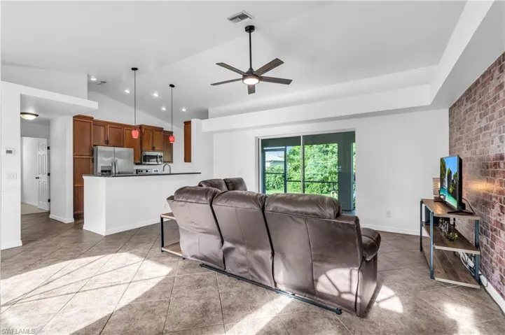 Tiled living room with vaulted ceiling, brick wall, and ceiling fan