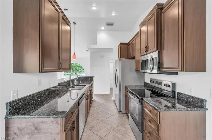 Kitchen with light tile patterned flooring, stainless steel appliances, dark stone counters, and sink