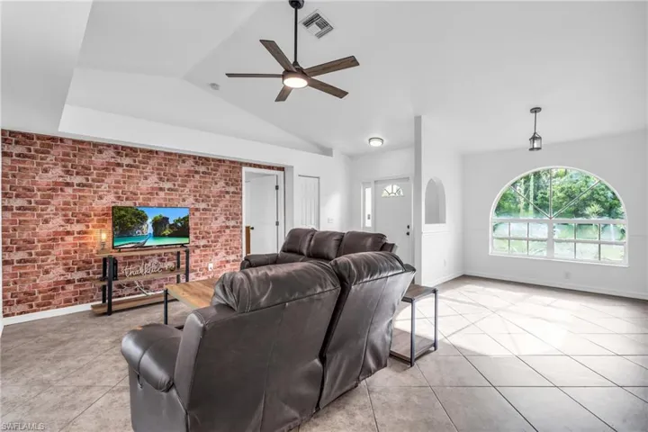 Tiled living room featuring ceiling fan, brick wall, and vaulted ceiling