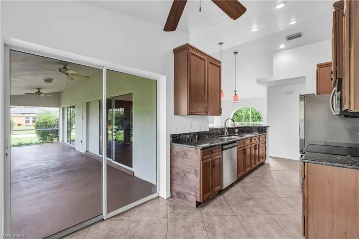 Kitchen featuring appliances with stainless steel finishes, ceiling fan, dark stone countertops, and sink