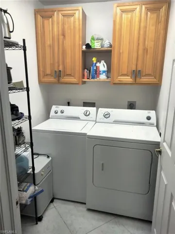 Laundry room featuring washing machine and dryer, light tile patterned floors, and cabinets