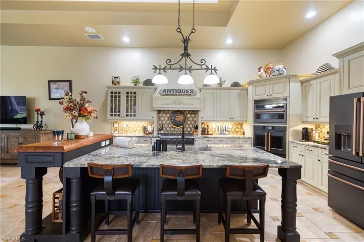 Dual tone kitchen featuring high end black refrigerator, a breakfast bar, light stone counters, and dual tone cabinetry
