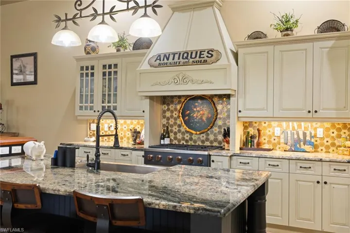 Dual tone kitchen featuring light stone counters, a breakfast bar, stainless steel gas cooktop, hanging light fixtures, and glass fronted cabinets