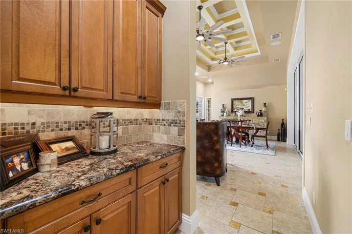 Kitchen featuring dark stone countertops, a raised ceiling, wood finish cabinetry, ceiling fan, and stone tile floors