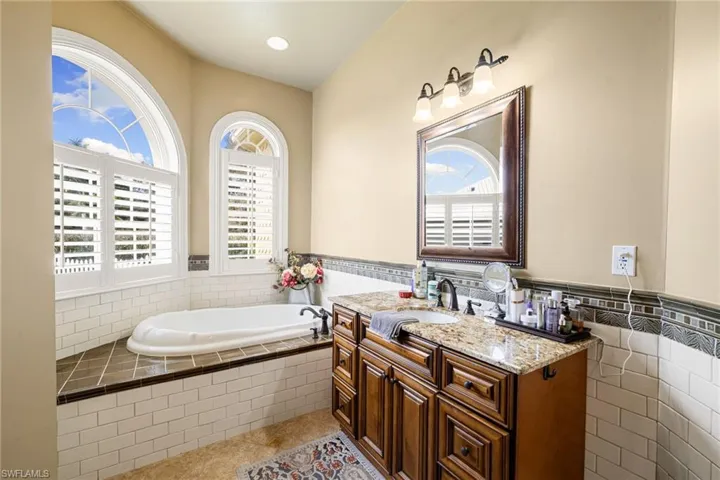 Bathroom with vanity, a bath, tile walls, a wainscoted wall, and light tile patterned flooring