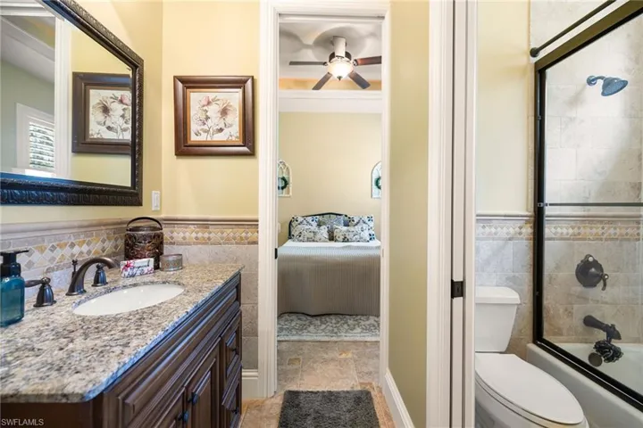 Ensuite bathroom featuring vanity, enclosed tub / shower combo, a ceiling fan, a wainscoted wall, and tile walls