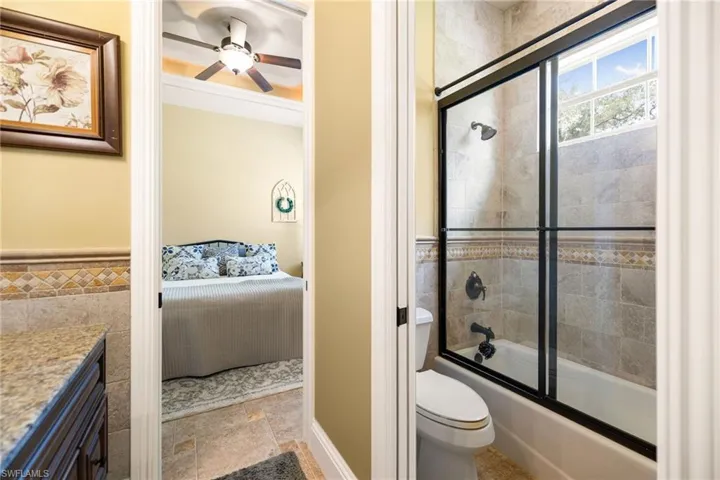 Full bathroom with vanity, ensuite bathroom, bath / shower combo with glass door, tile walls, and ceiling fan