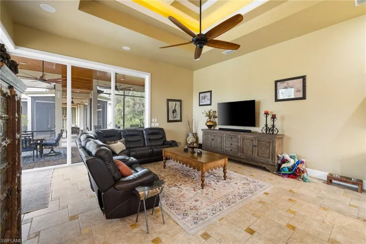Living room featuring ceiling fan, a tray ceiling, and light stone finish floors