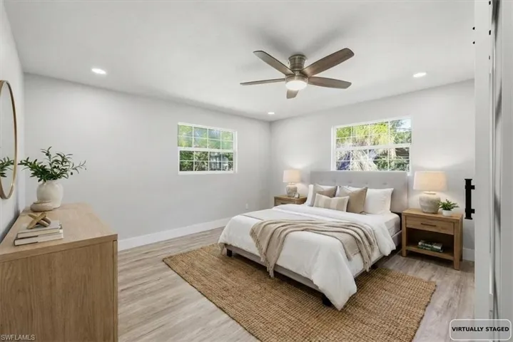 Bedroom 1 with light wood-style floors, a ceiling fan, multiple windows, and recessed lighting- virtually stage