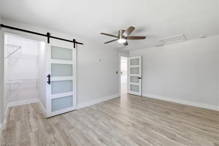 Unfurnished bedroom 2 featuring a barn door, light wood-style floors, a ceiling fan, and a walk in closet