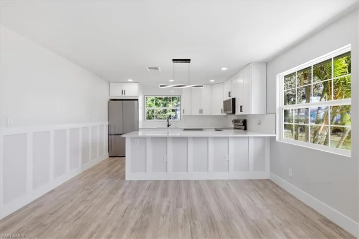 Kitchen with white cabinets, stainless steel appliances, a peninsula, decorative light fixtures, and light wood-type flooring