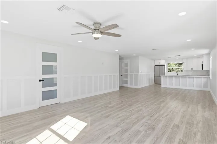 Unfurnished living room featuring a ceiling fan, light wood-style flooring, recessed lighting, and wainscoting