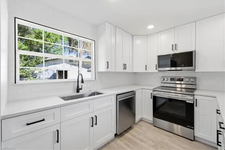Kitchen with white cabinetry, stainless steel appliances, light stone countertops, backsplash, and recessed lighting