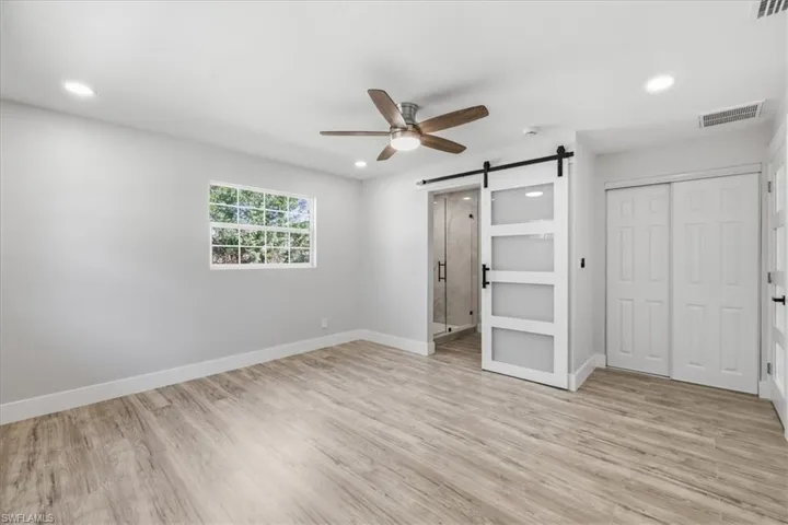 Unfurnished bedroom 1 with a barn door, light wood-style flooring, ceiling fan, recessed lighting, and a closet