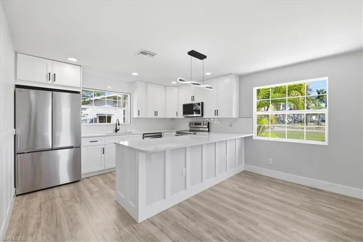 Kitchen with stainless steel appliances, white cabinets, pendant lighting, and a peninsula