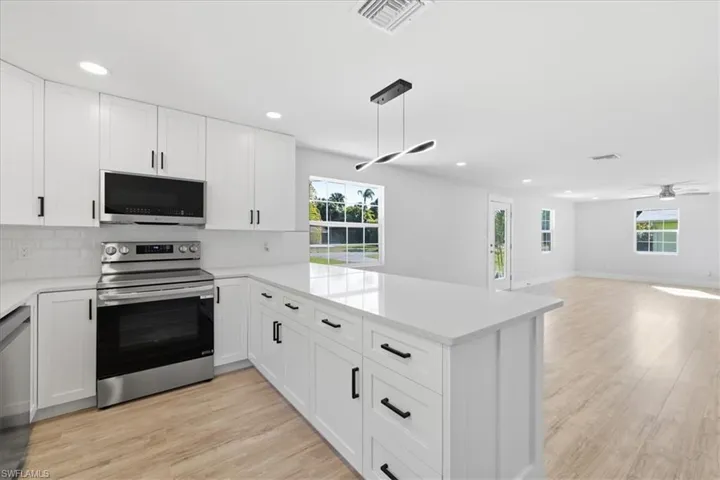 Kitchen featuring light wood-style flooring, stainless steel appliances, a peninsula, and white cabinetry