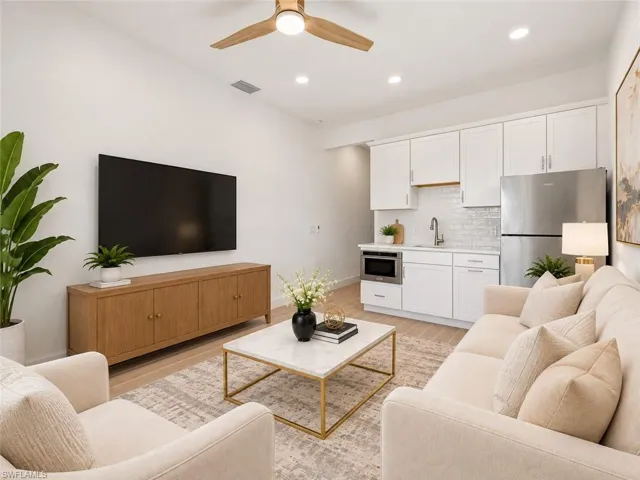 Virtually staged kitchenette featuring white cabinetry, subway tile backsplash, stainless steel refrigerator, and integrated microwave, complemented by recessed lighting and a wood-finish ceiling fan