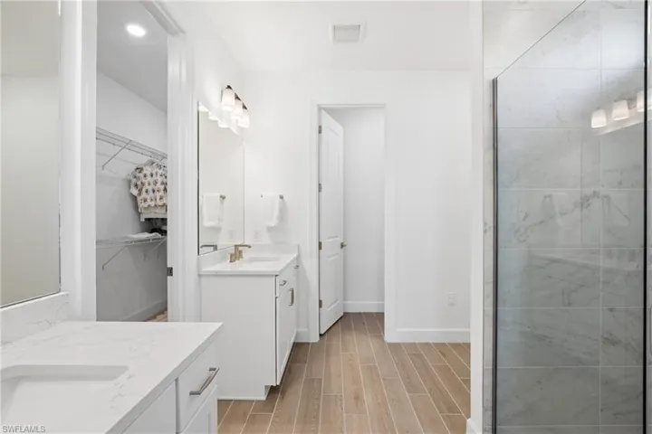 Dual vanity with white cabinetry and integrated sinks, glass-enclosed shower with tile surround, and wood-look flooring