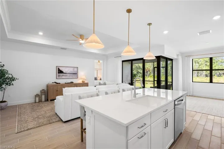 Spacious open-concept interior featuring light tile flooring, a kitchen island with integrated sink, recessed lighting, and large windows